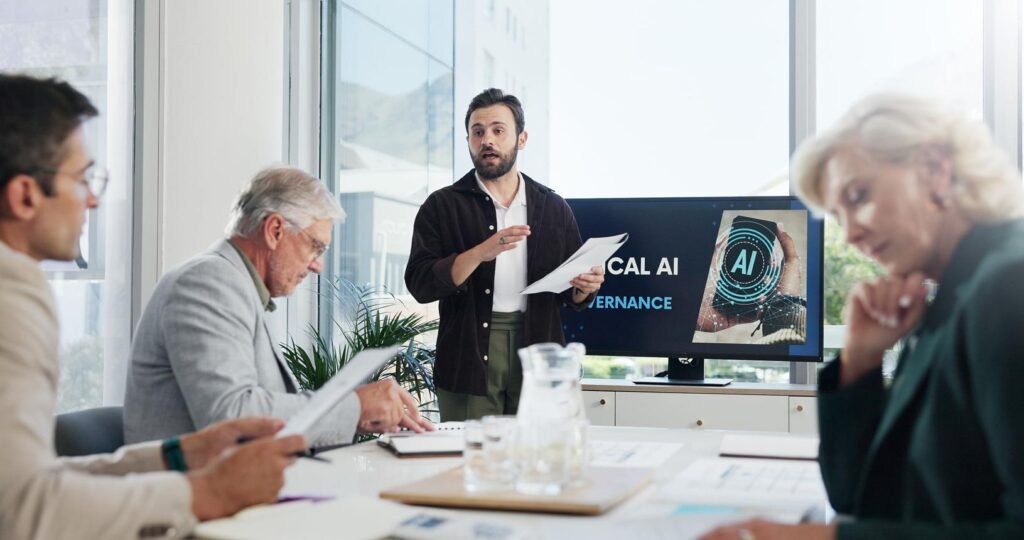 Presenter leads a meeting in a bright conference room while others review documents, with an AI-themed slide on the screen behind him.