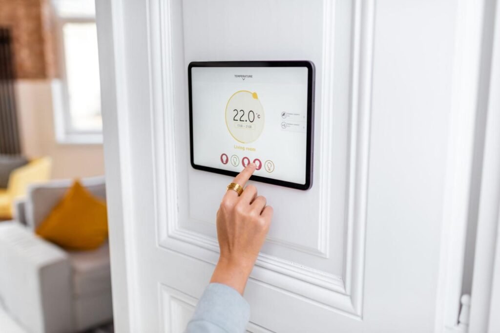 Touchscreen smart thermostat mounted on a white wall, displaying 22.0°C, as a person taps the screen.