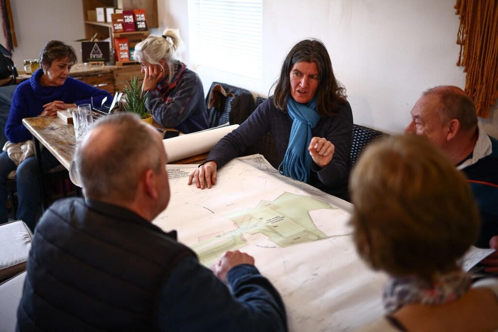 Six adults seated around a large table covered with maps, discussing plans in a bright, casual room.