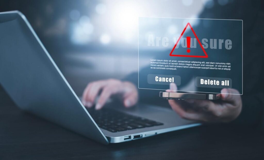 Laptop with a translucent security warning overlay showing a red exclamation triangle and options 'Cancel' and 'Delete all'