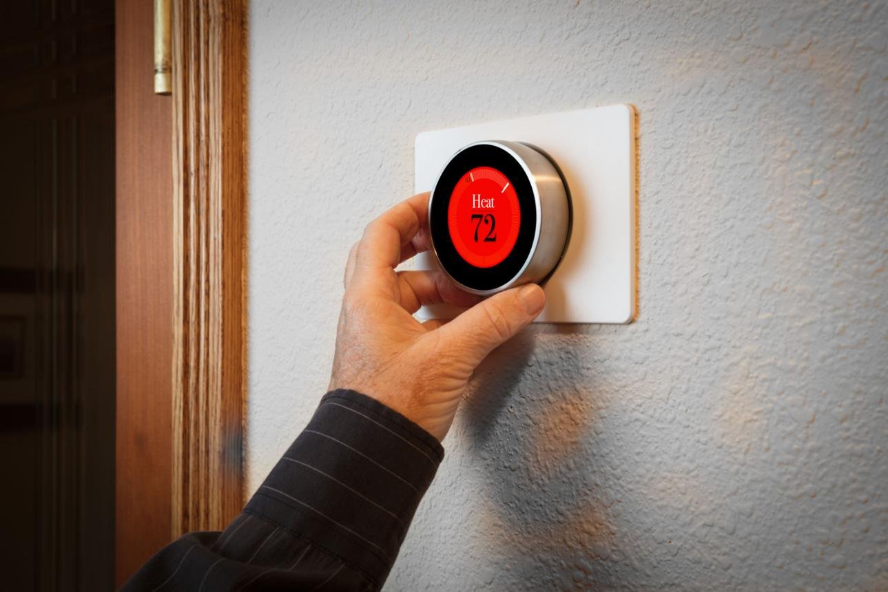 Hand turning a circular wall thermostat; red display reads Heat 72°F.