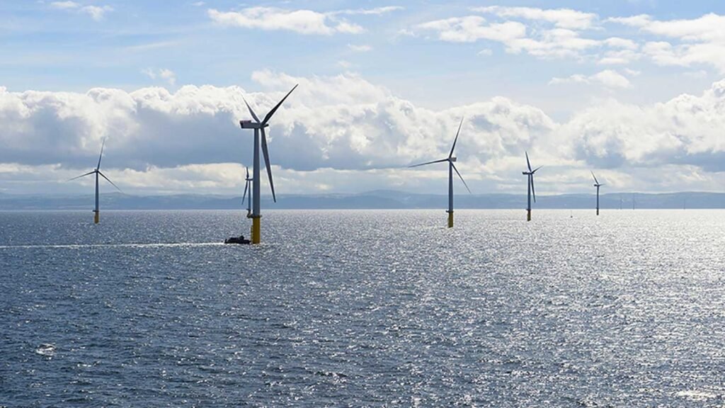 Offshore wind farm with several wind turbines standing in the sea under a sunny, partly cloudy sky.