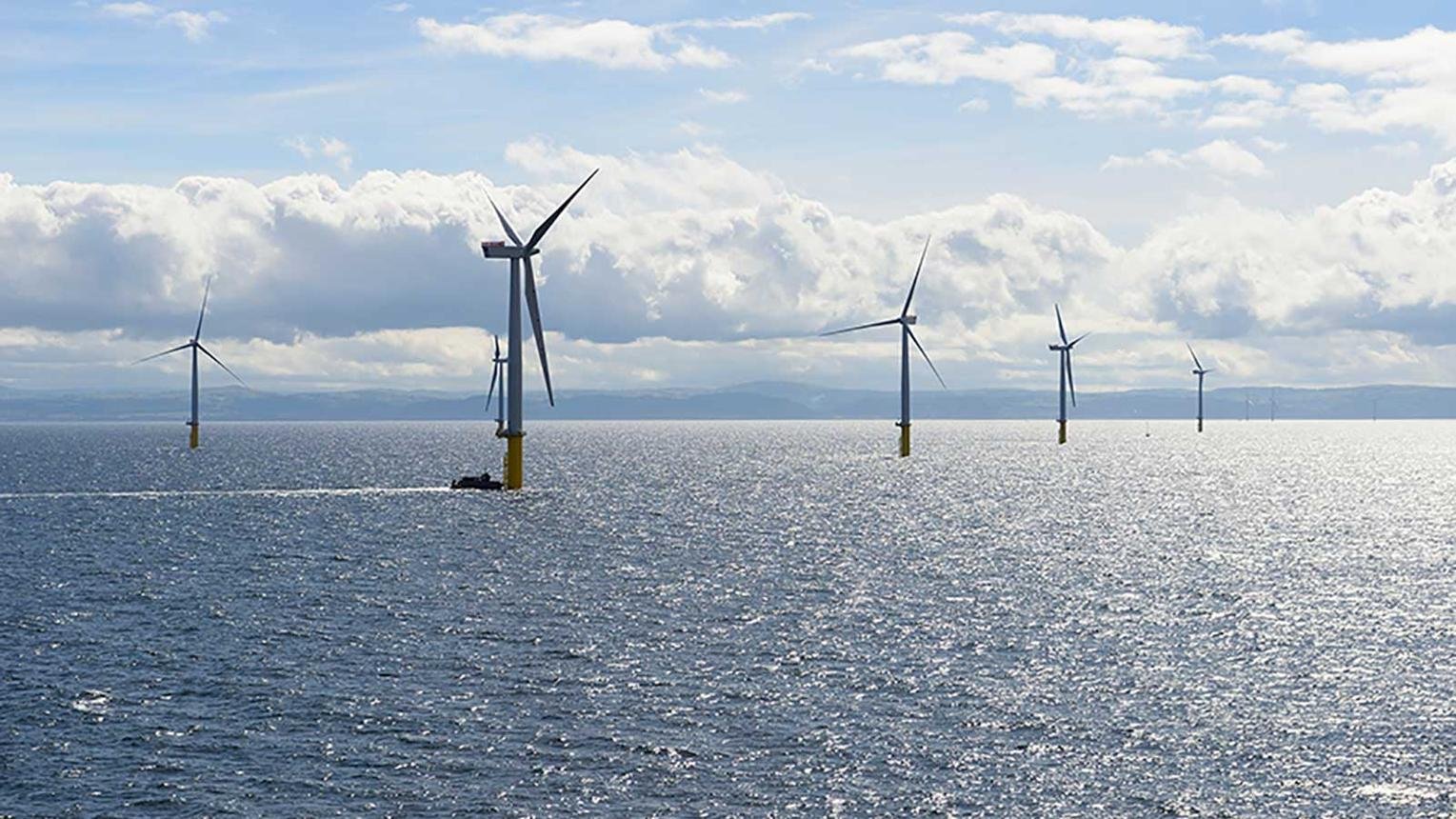 Offshore wind farm with several wind turbines standing in the sea under a sunny, partly cloudy sky.
