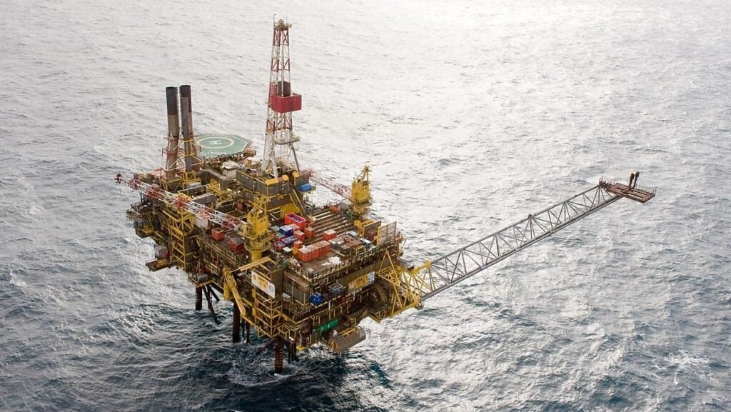 Offshore oil platform with a long drilling arm, cranes, and a helipad sitting in open sea. (oil rig)