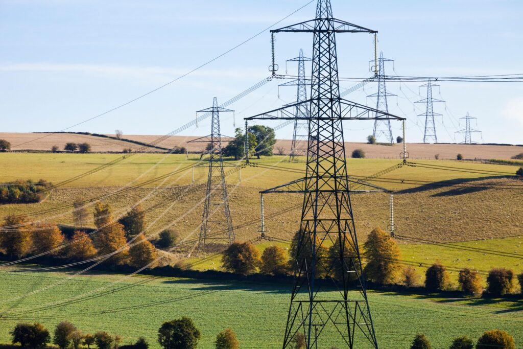 Row of electrical transmission towers spanning a rural landscape with fields and trees.
